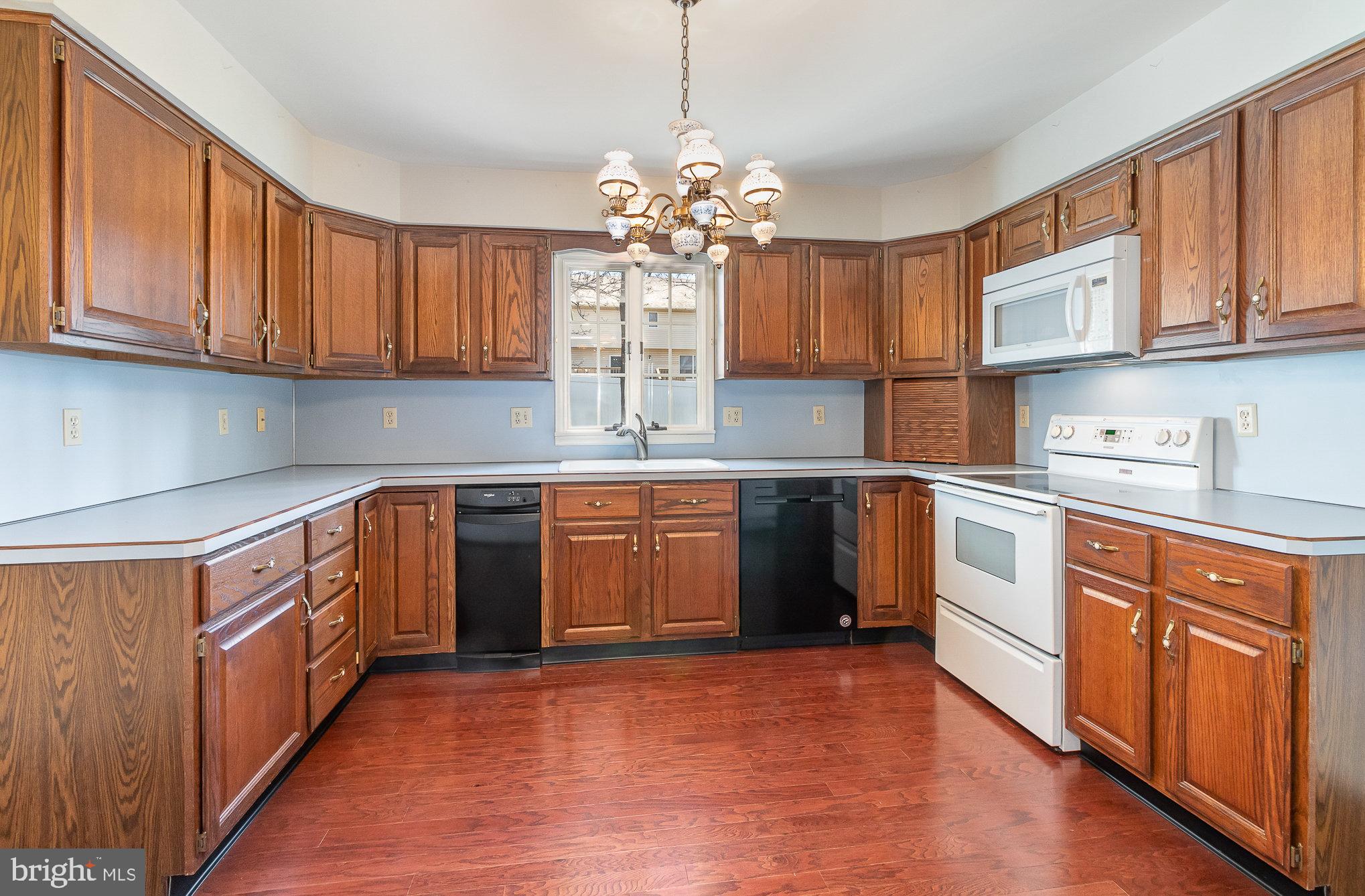 Kitchen with extensive wood cabinetry, white appliances, and reddish hardwood flooring.