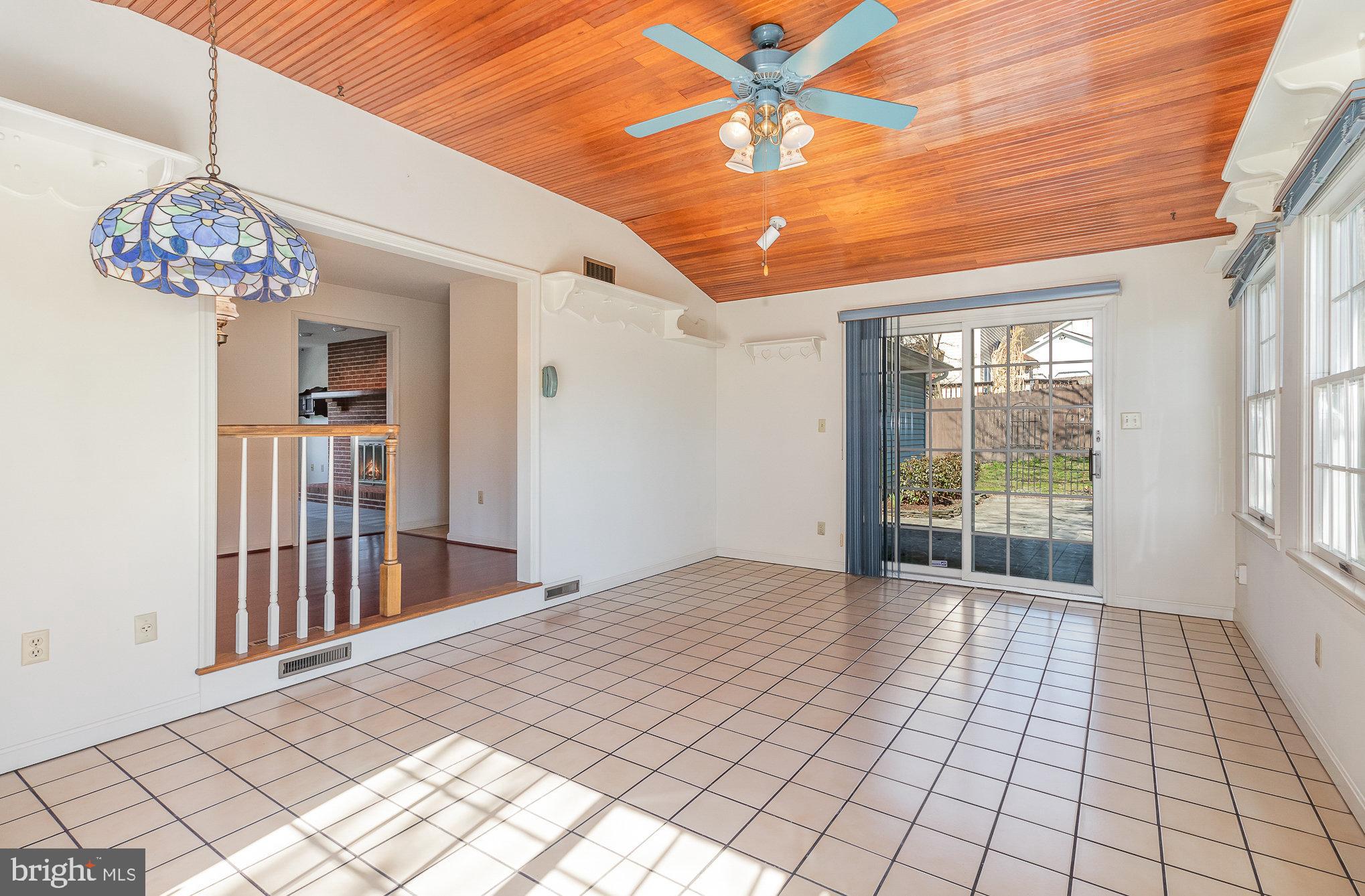 Vacant sunroom with a wood-plank ceiling, tiled floor, and sliding glass door to the patio.