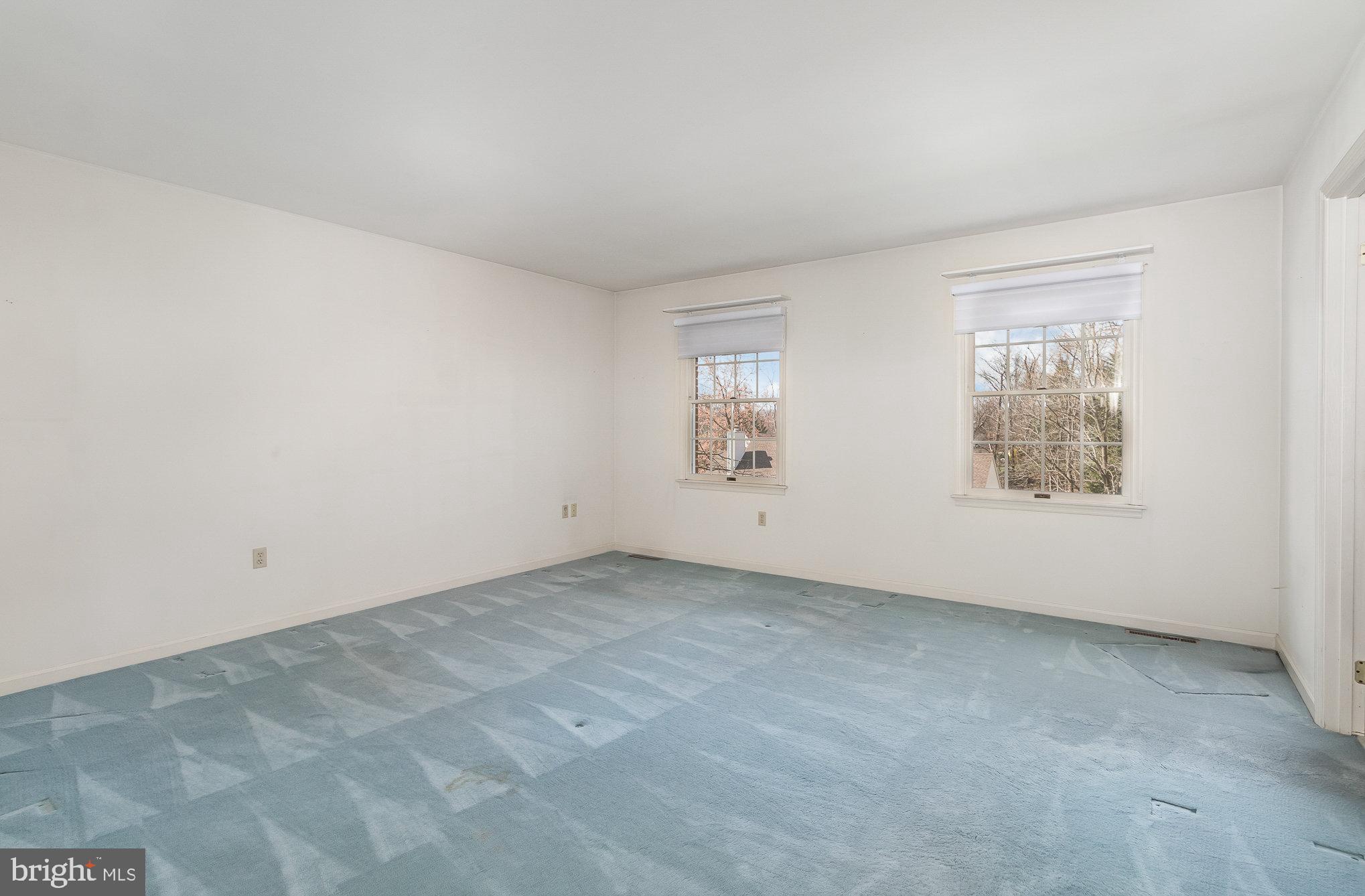 Empty room with blue-gray carpet, white walls, and two windows with blinds.