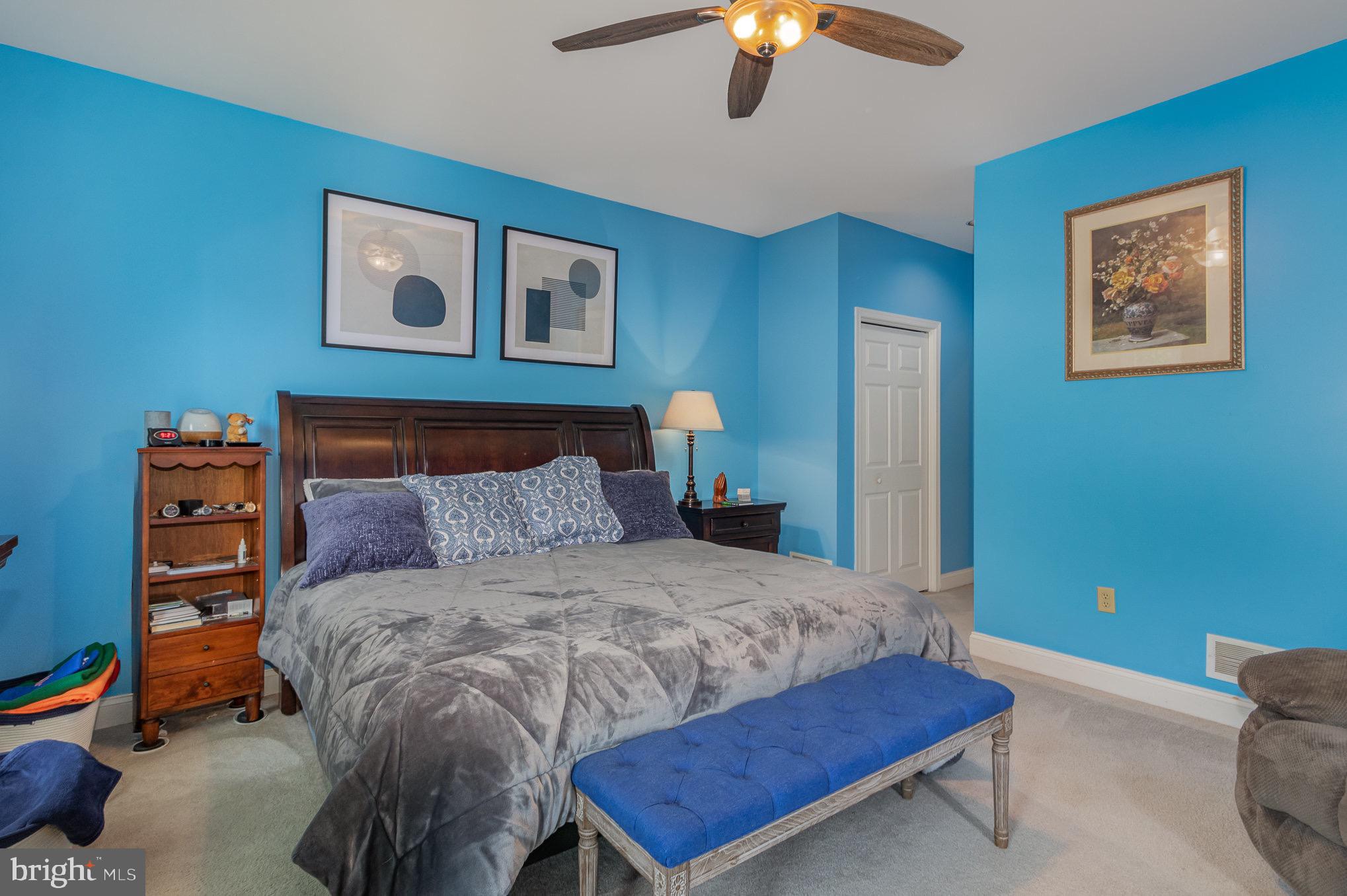 Bedroom with bright blue walls, a dark wood bed, gray bedding, and a blue upholstered bench.