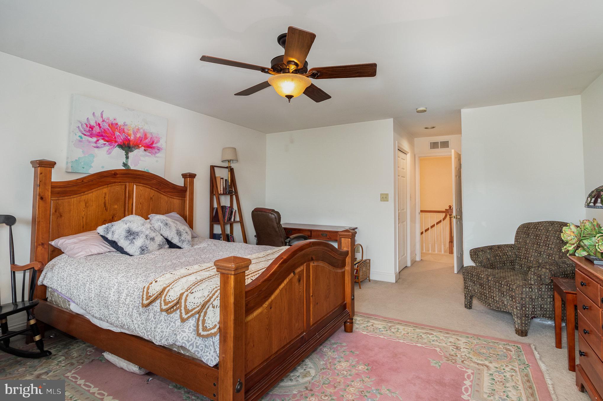 Furnished bedroom with a large wooden bed, floral rugs, and a ceiling fan.