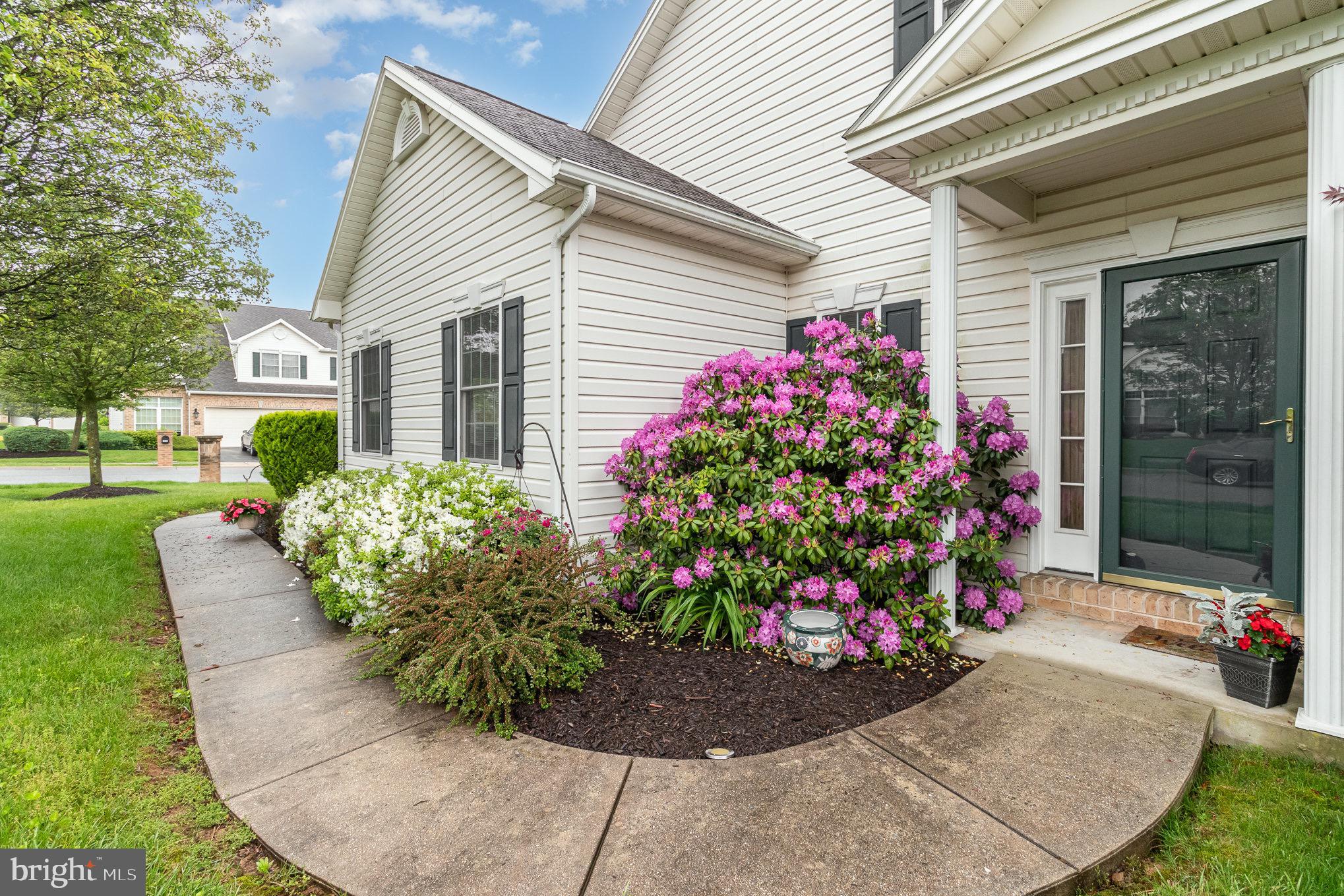 Home entrance with a dark green door, curved walkway, and blooming pink azaleas.