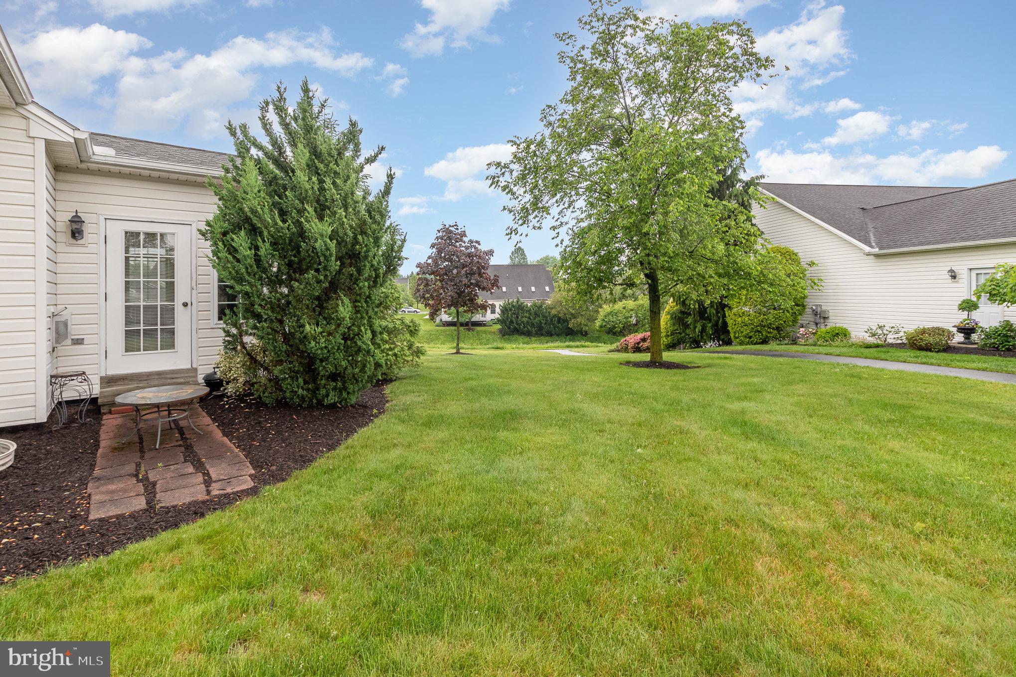 Backyard lawn with a brick patio, mature trees, and neighboring homes.