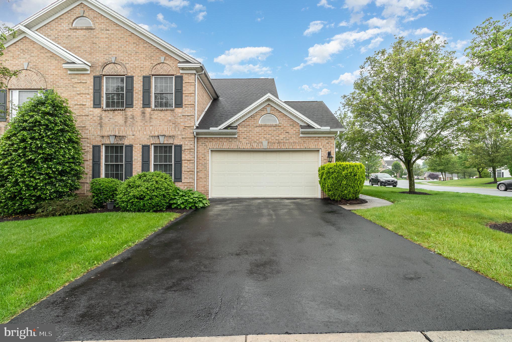 Two-story brick home with dark shutters, an attached garage, and a wide asphalt driveway.