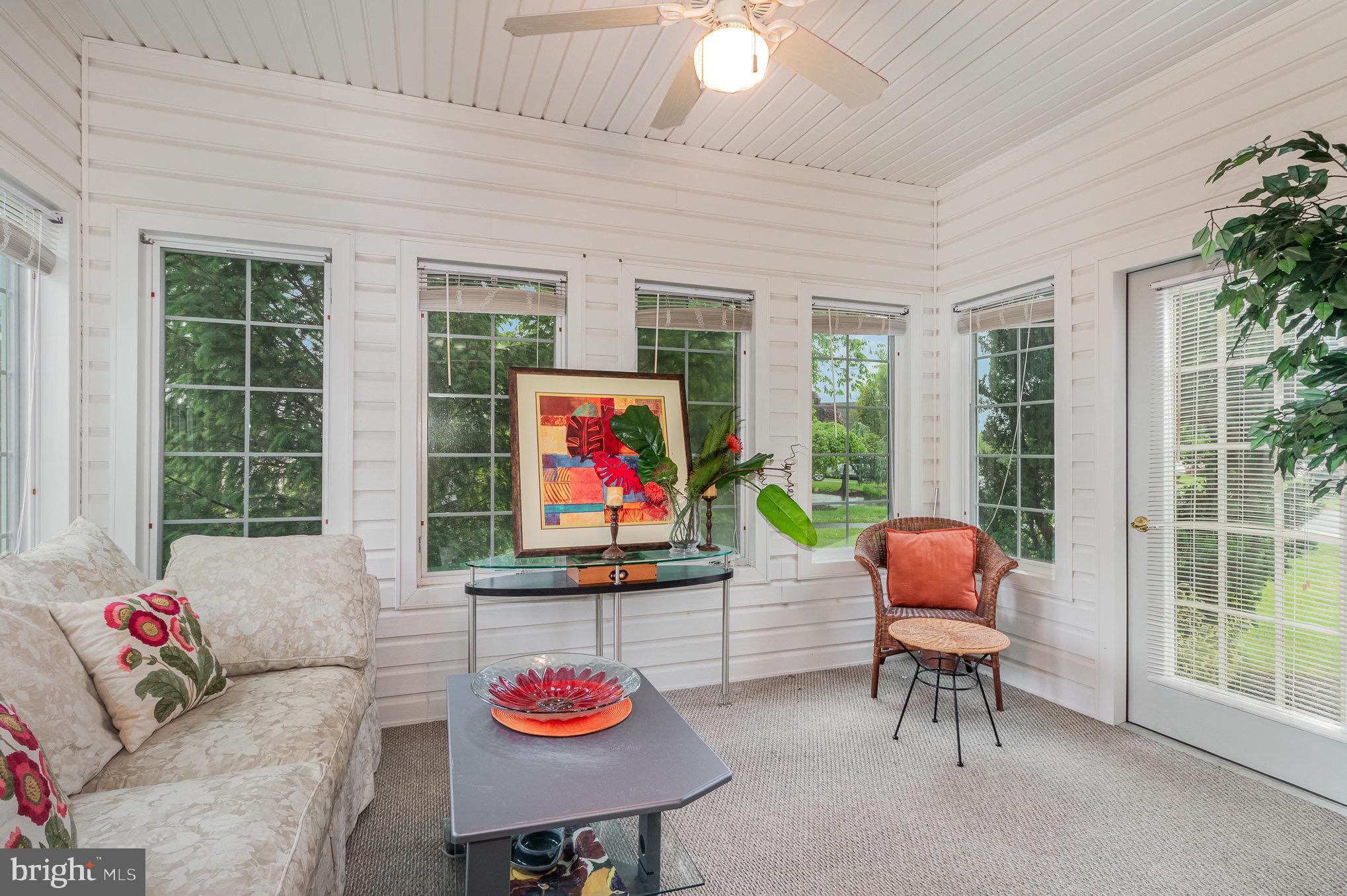 Sunroom with windows on several sides, white paneled walls, and a furnished seating area.
