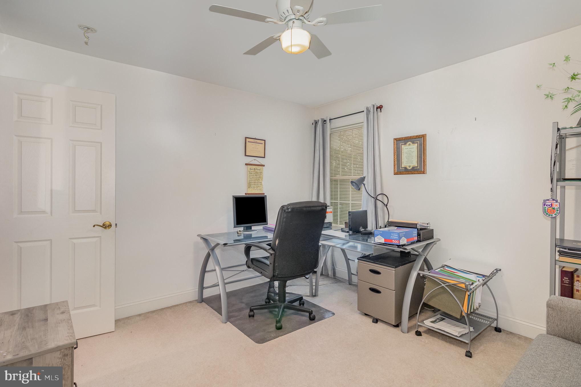 Furnished home office with a glass desk, black chair, and window with gray curtains.