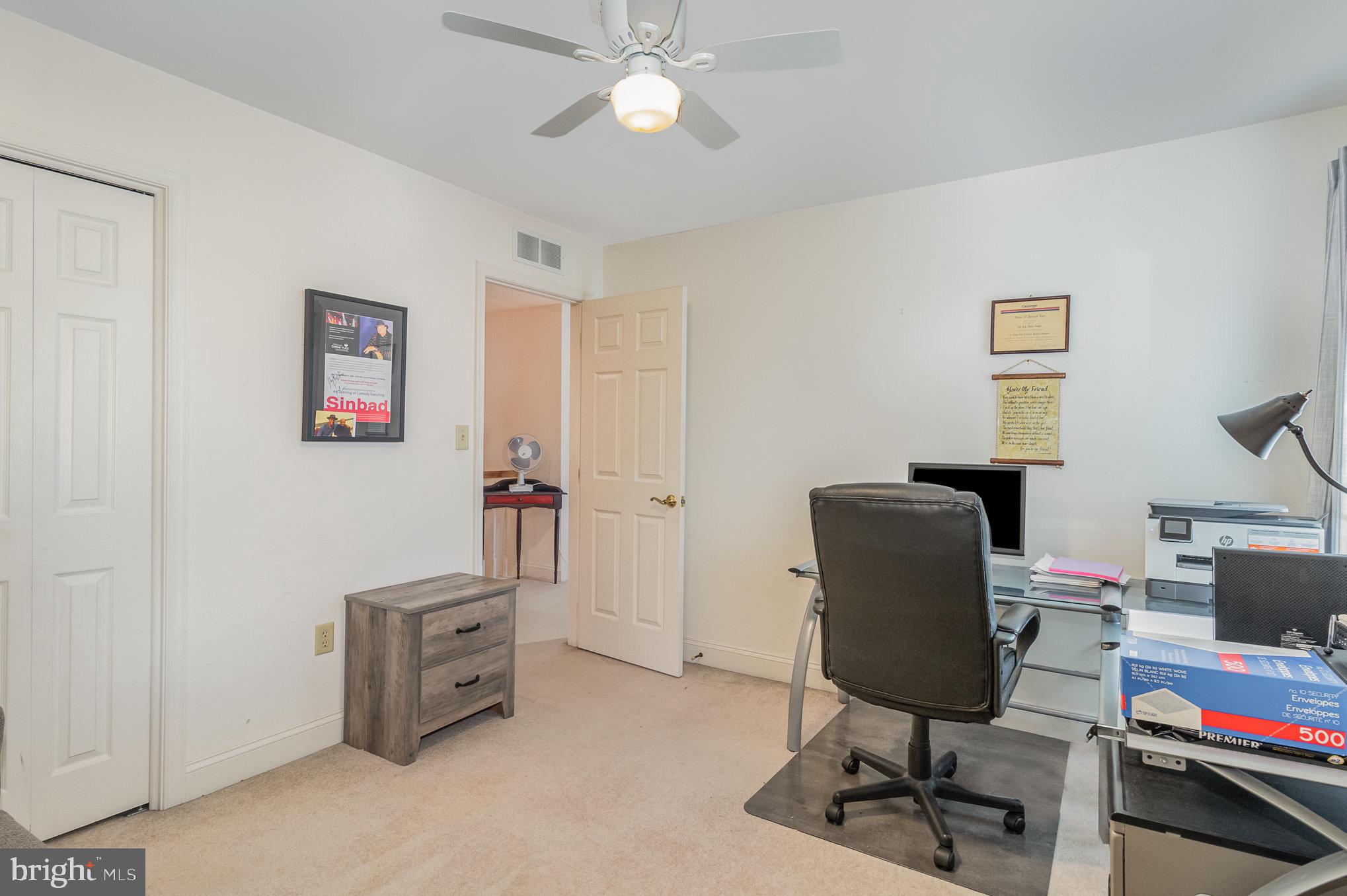 Home office with a glass desk, black chair, printer, and open doorway to an adjoining room.