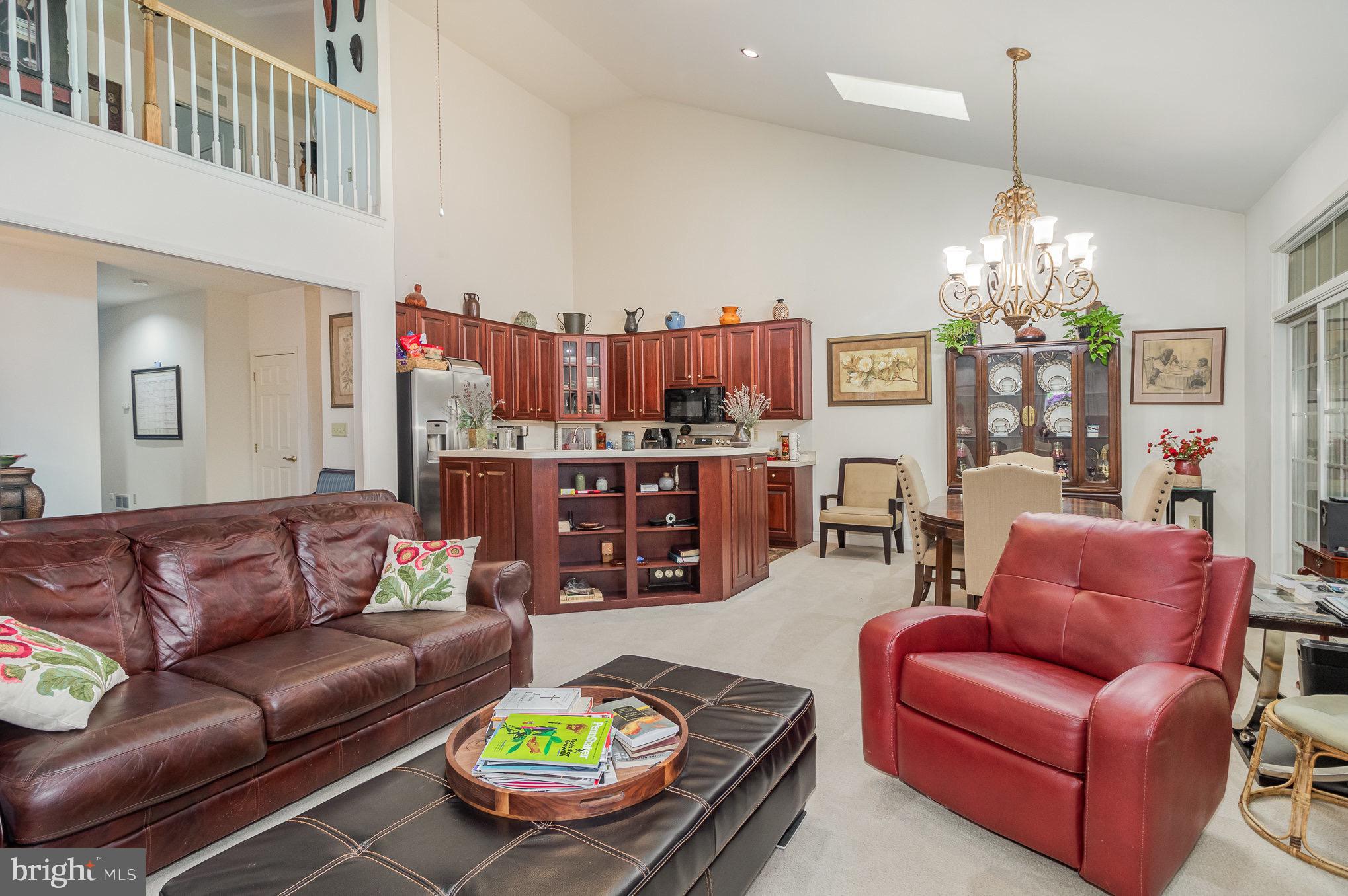 Open living and dining area with a vaulted ceiling, reddish wood kitchen cabinets, and leather seating.