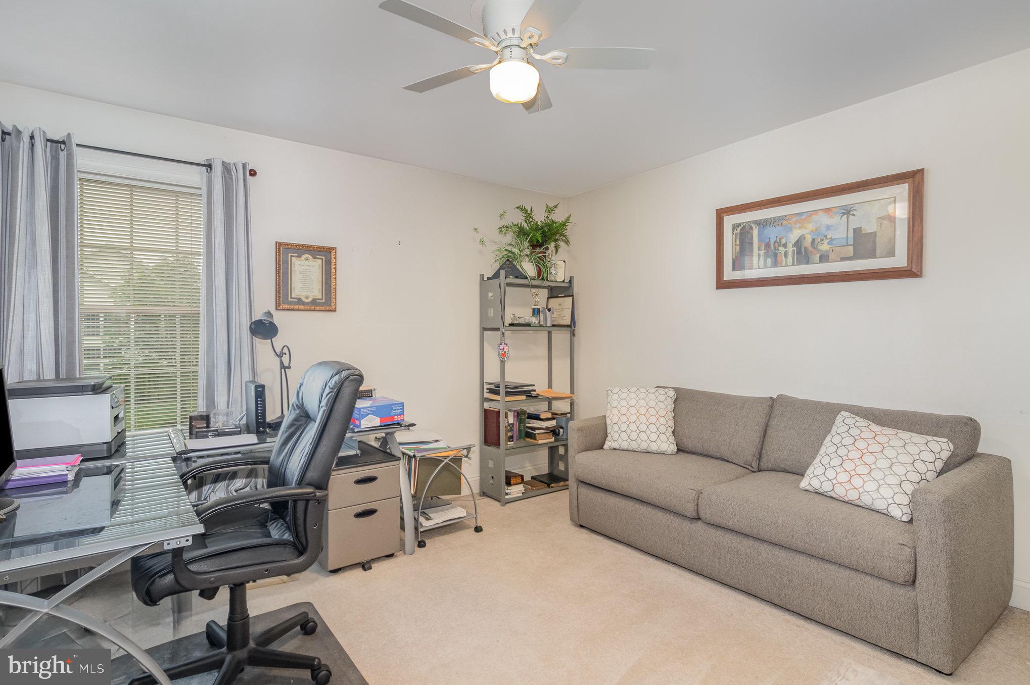 Home office with a glass desk and black chair beside a gray sofa.