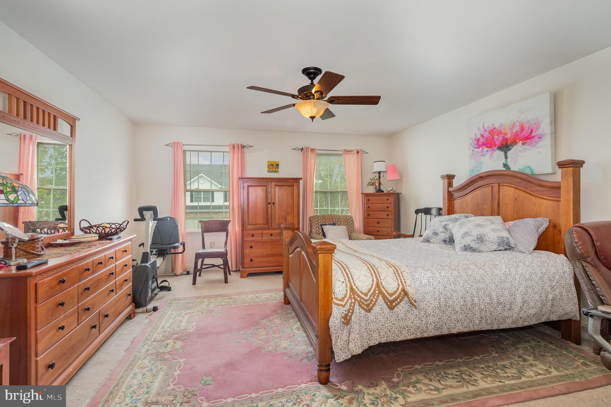 Furnished bedroom with a large wooden bed, matching dressers, pink curtains, and floral rugs.