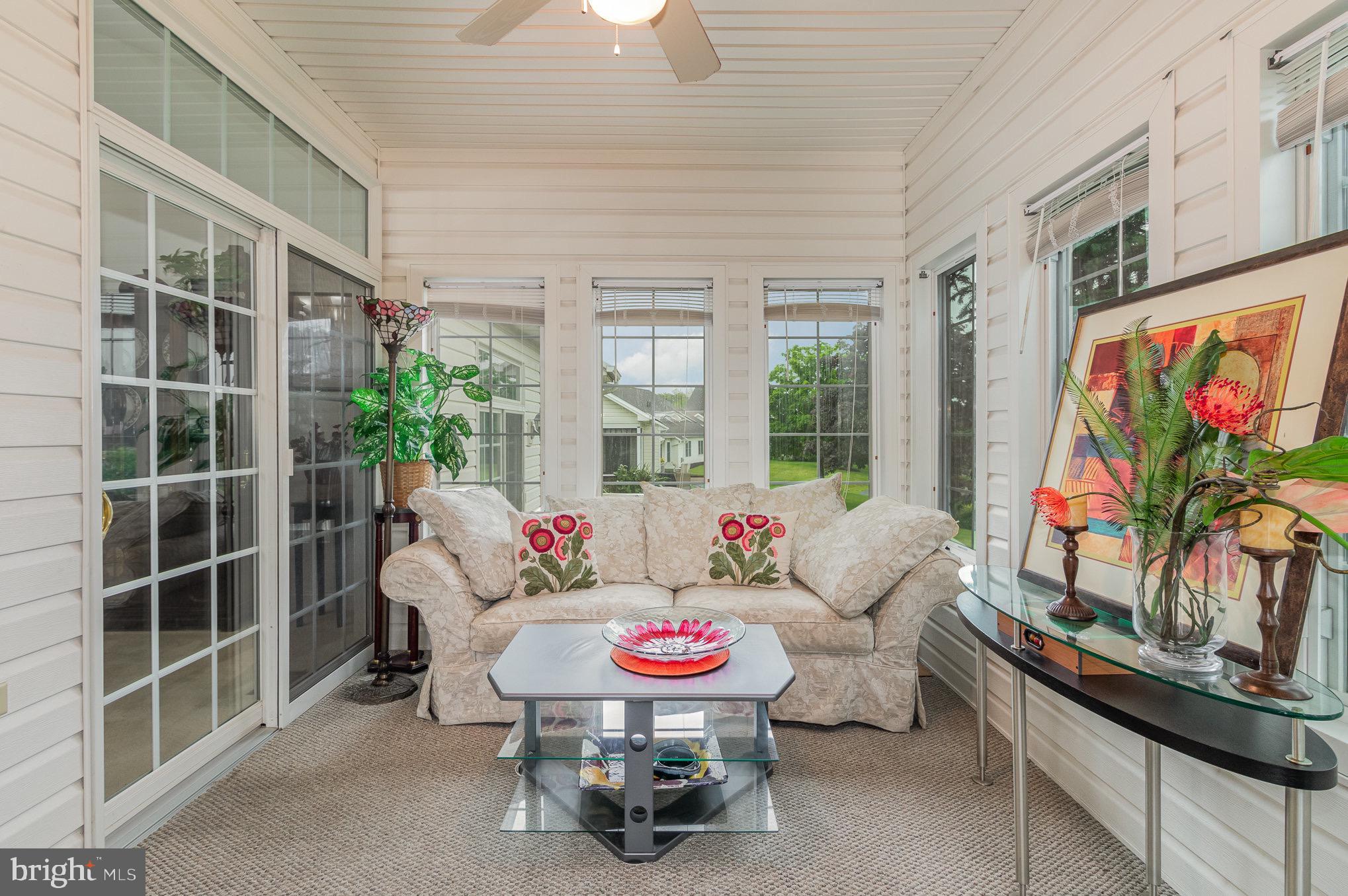 Furnished sunroom with a beige sofa, large windows, and views of the lawn.
