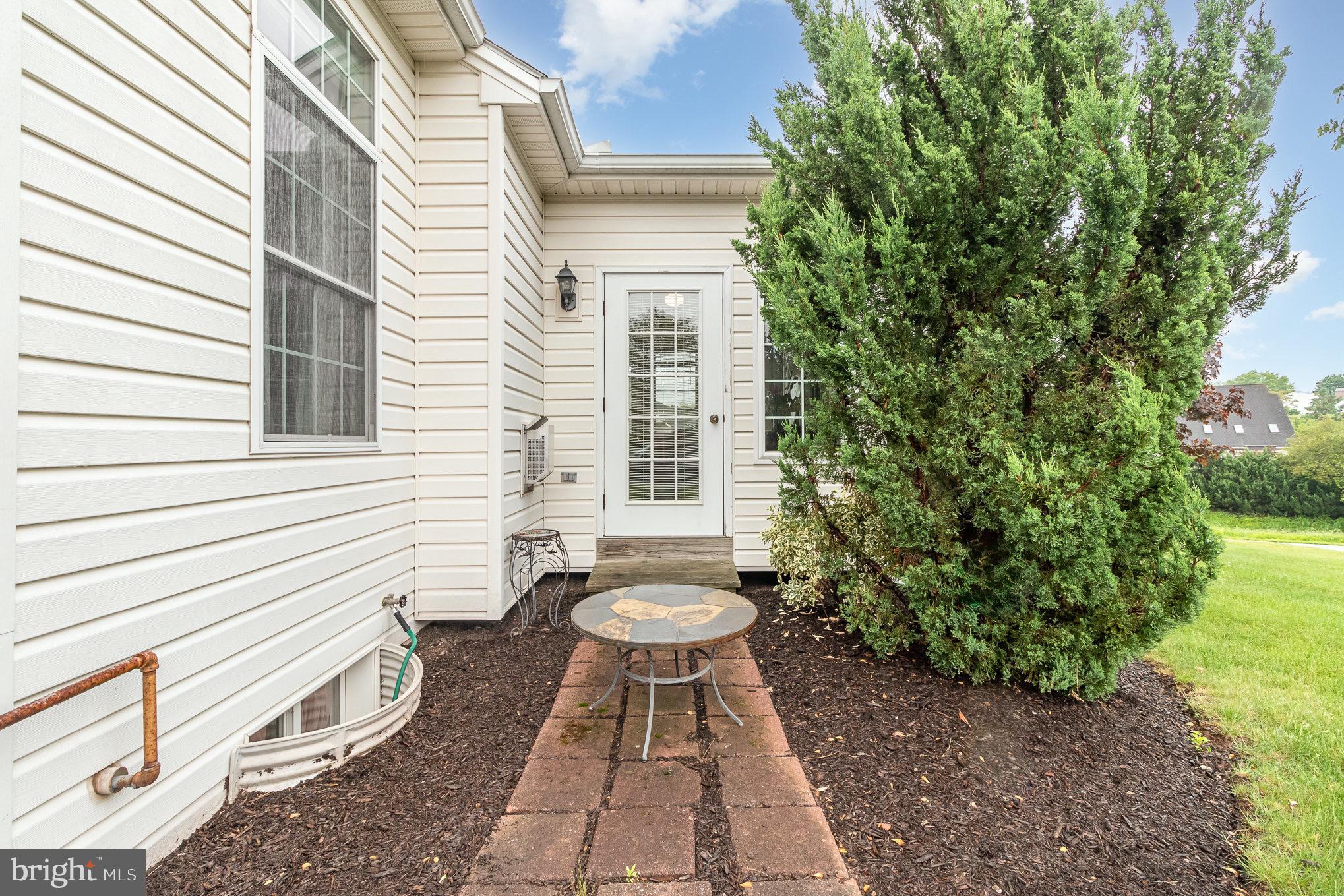 Rear patio with a brick walkway, round table, and large evergreen shrub beside the home.