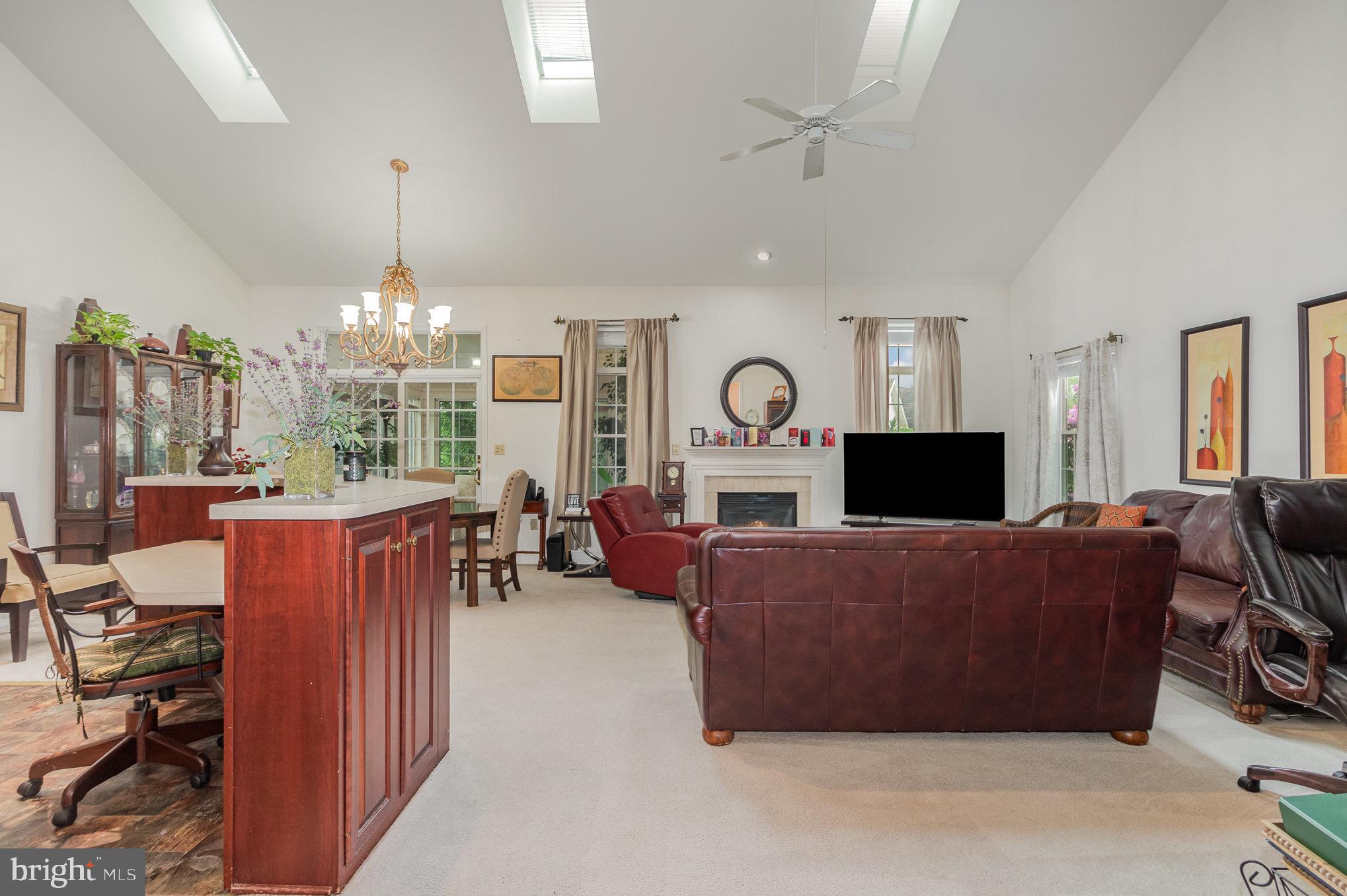 Furnished living room with vaulted skylit ceiling, fireplace, leather seating, and a large kitchen island.
