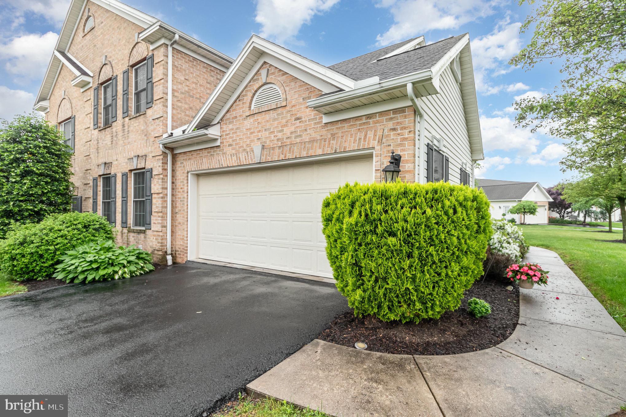 Two-story brick home with a white double garage, wide driveway, and landscaped front shrubs.