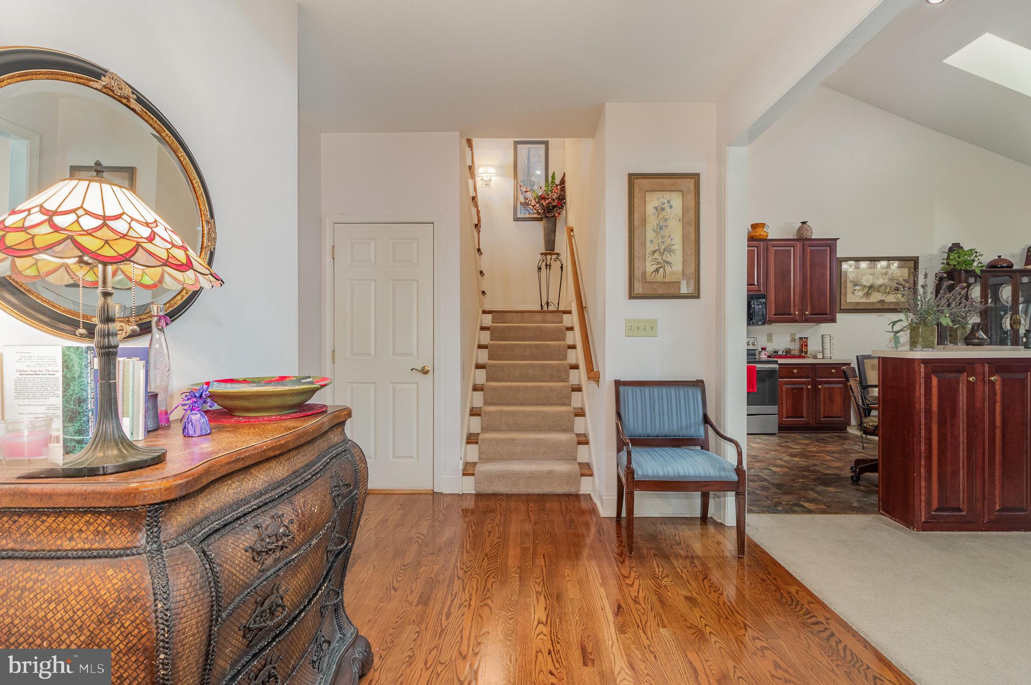 Foyer with carpeted stairs, hardwood floors, an ornate chest, and an adjoining kitchen.