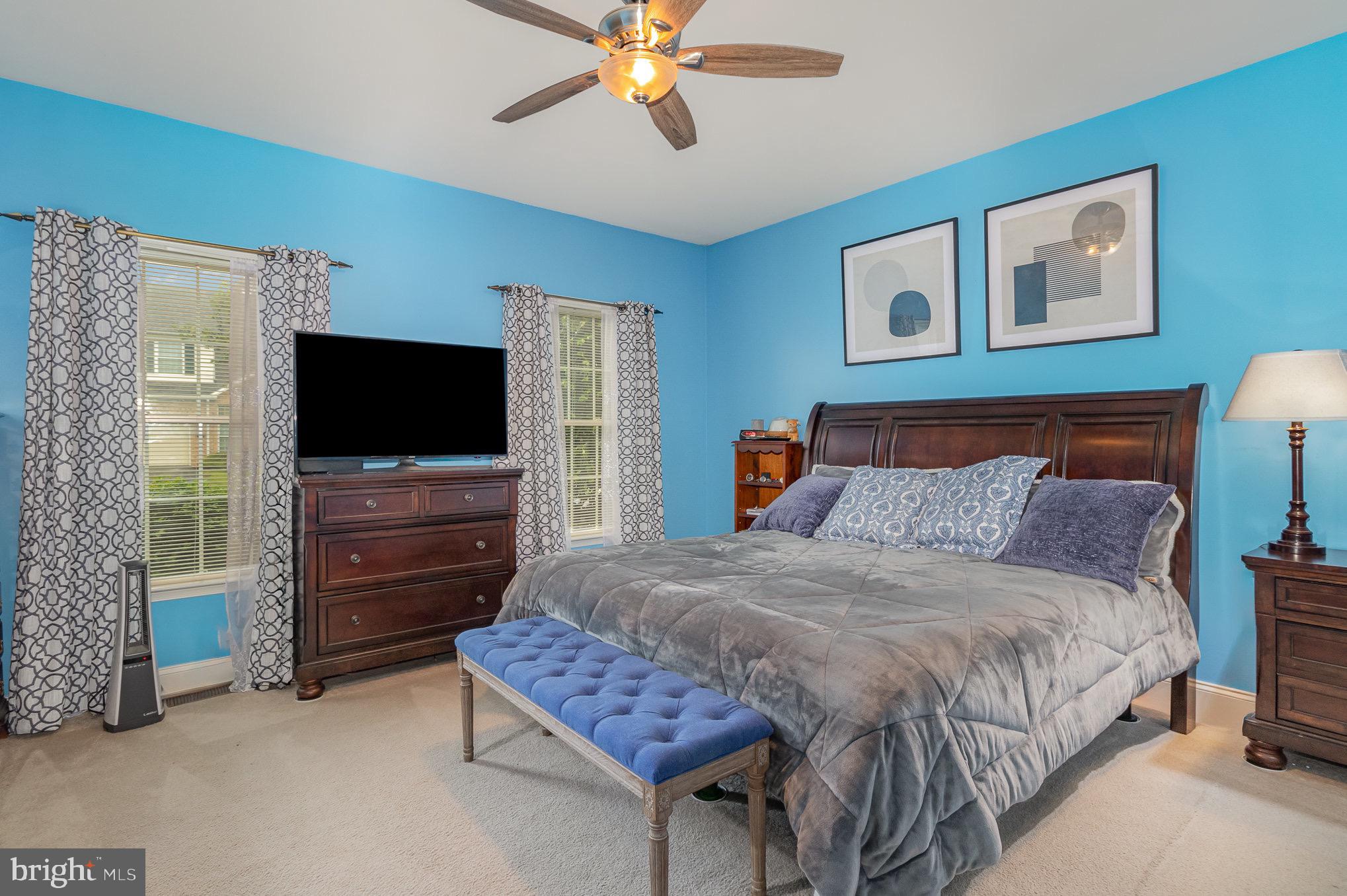 Furnished bedroom with bright blue walls, a large dark wood bed, and two windows.