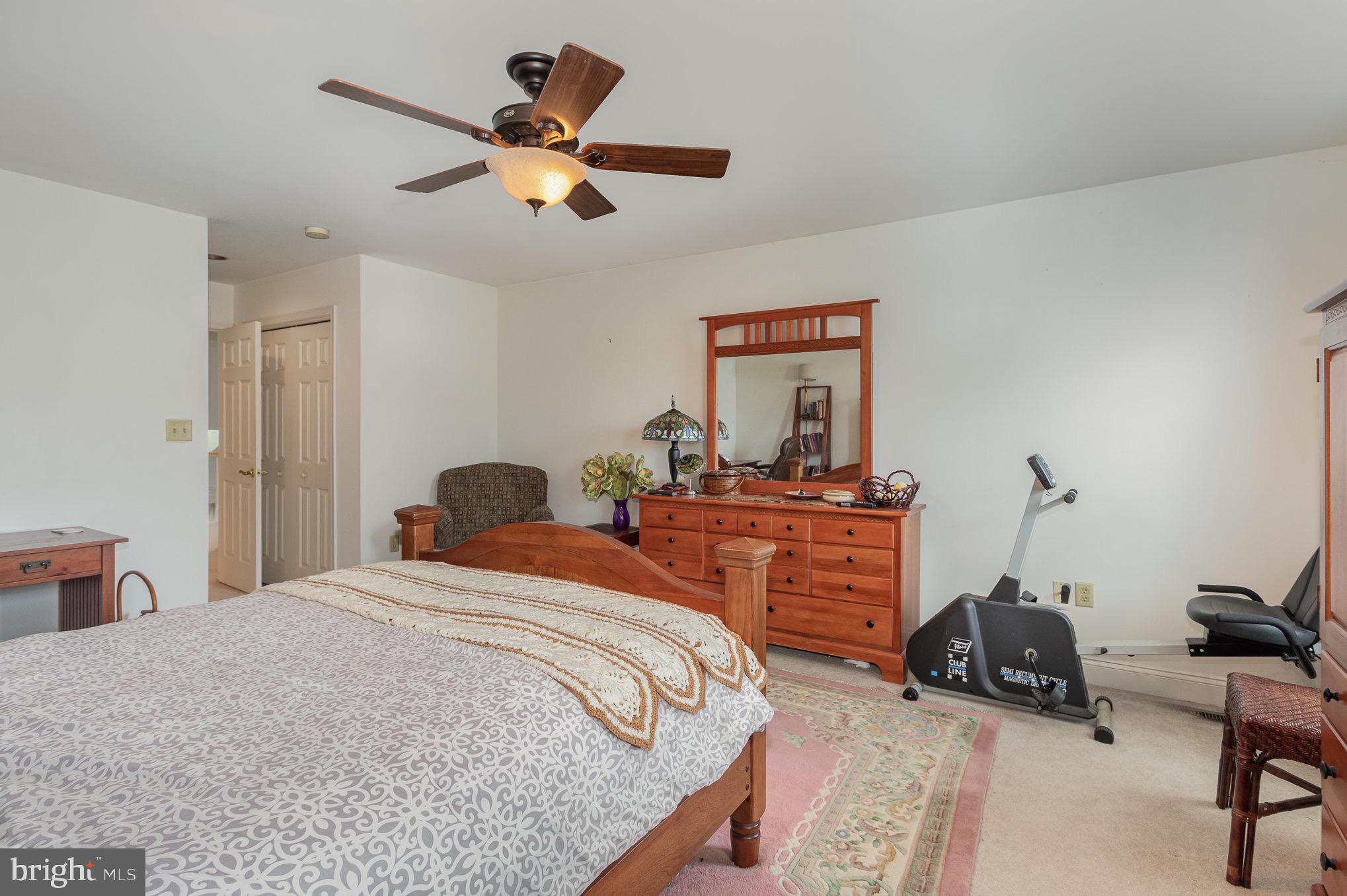 Furnished bedroom with a wooden bed and dresser, ceiling fan, and exercise bike.