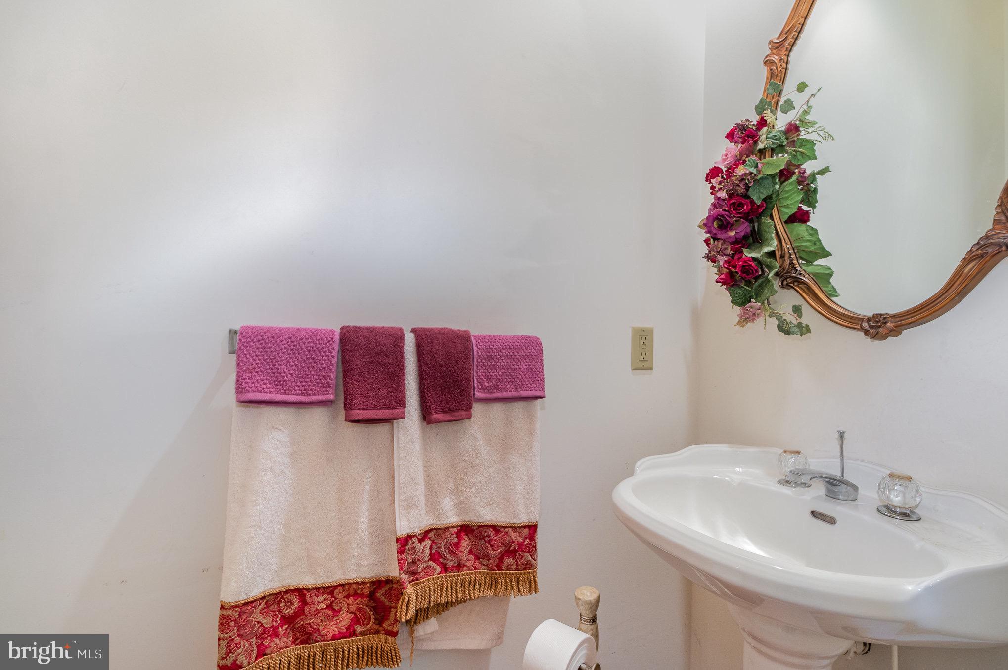 Bathroom sink beneath an ornate mirror, beside decorative pink and cream towels.