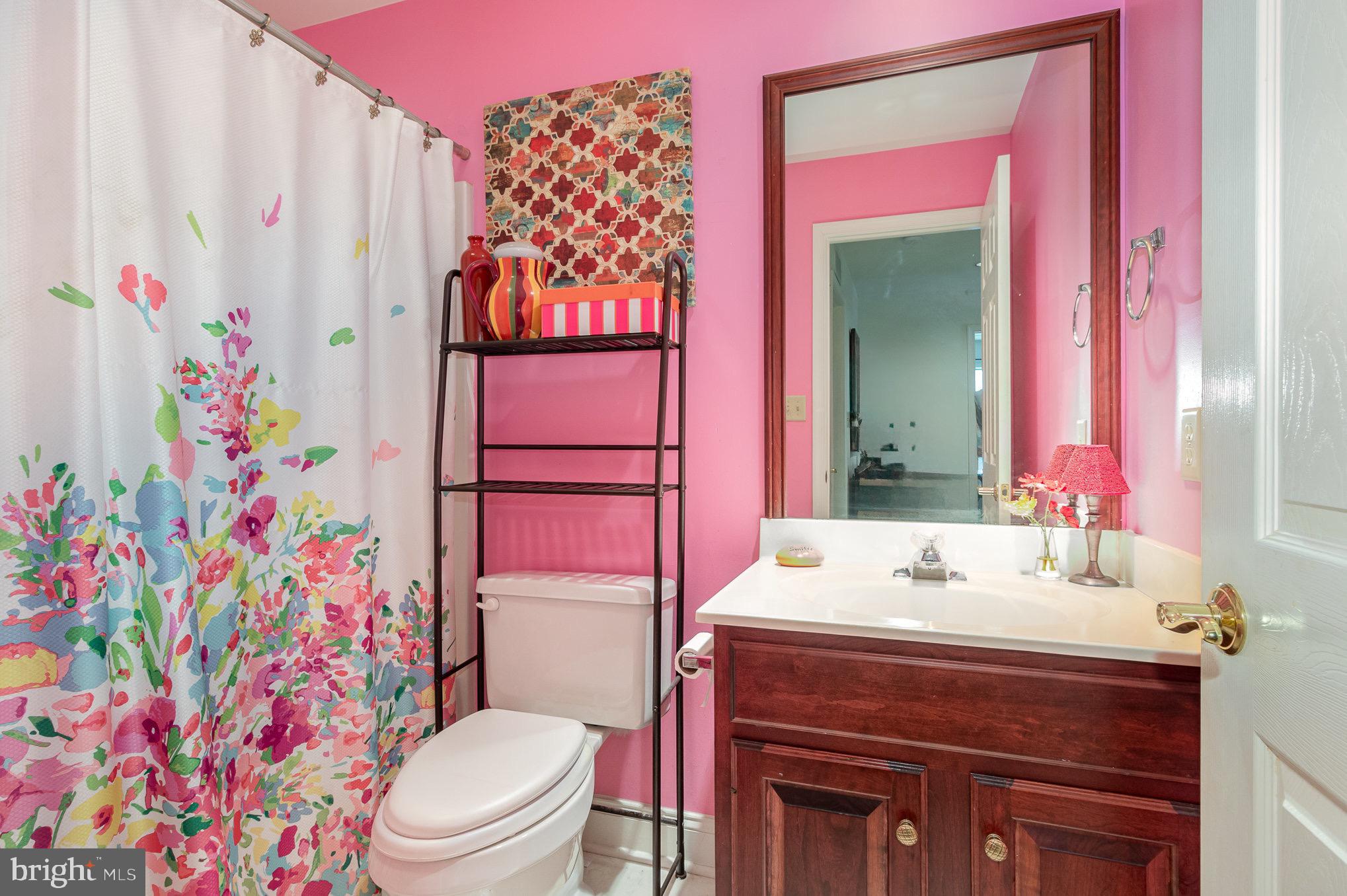 Pink bathroom with a floral shower curtain, white toilet, and dark wood vanity.