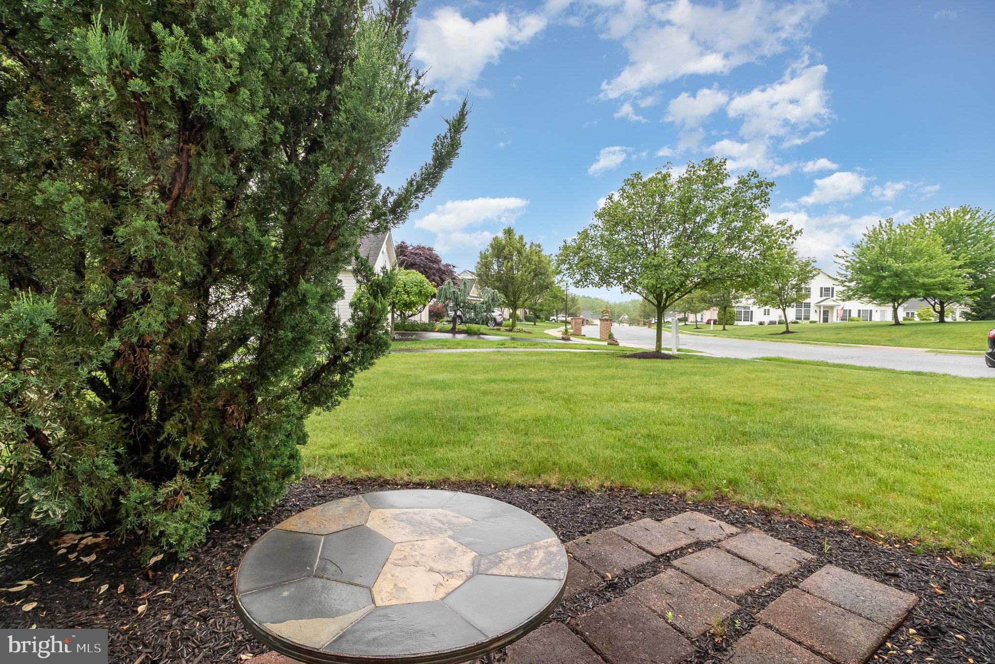 Backyard patio with a circular stone fire pit, lawn, mature trees, and neighboring homes.