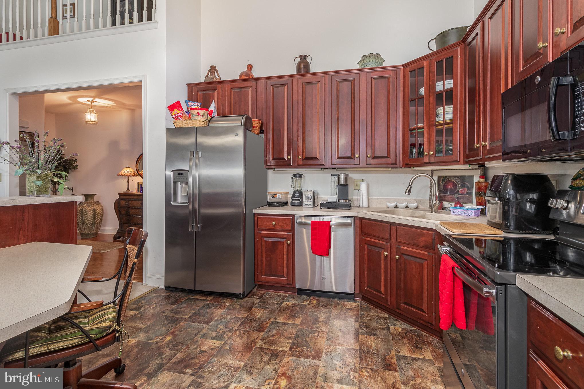 Kitchen with reddish-brown cabinetry, stainless steel appliances, and multicolored tile flooring.