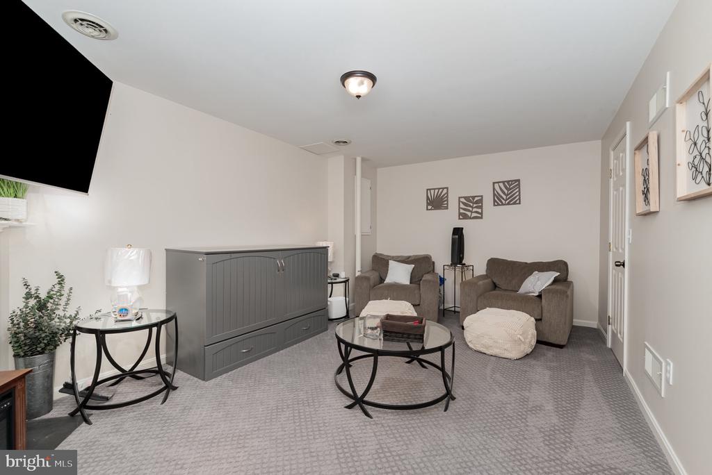 Furnished living room with gray carpet, two armchairs, a glass coffee table, and a wall-mounted TV.