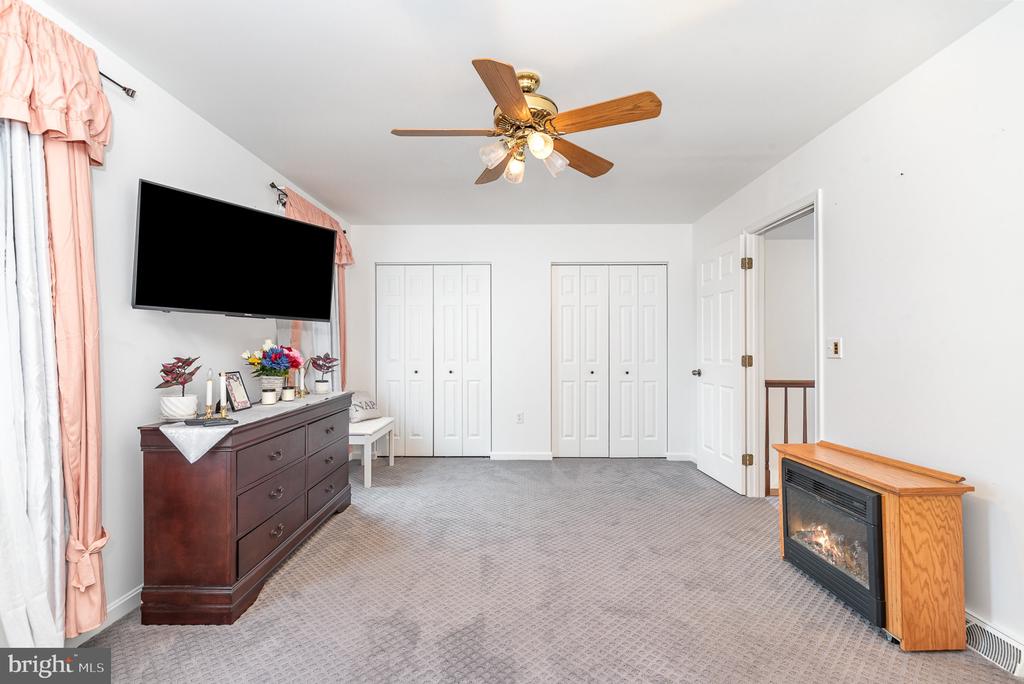 Bedroom with gray carpet, double closets, a ceiling fan, and an electric fireplace.