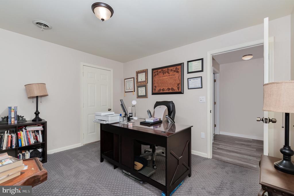 Furnished office with a dark desk, gray carpet, bookshelves, and framed certificates.