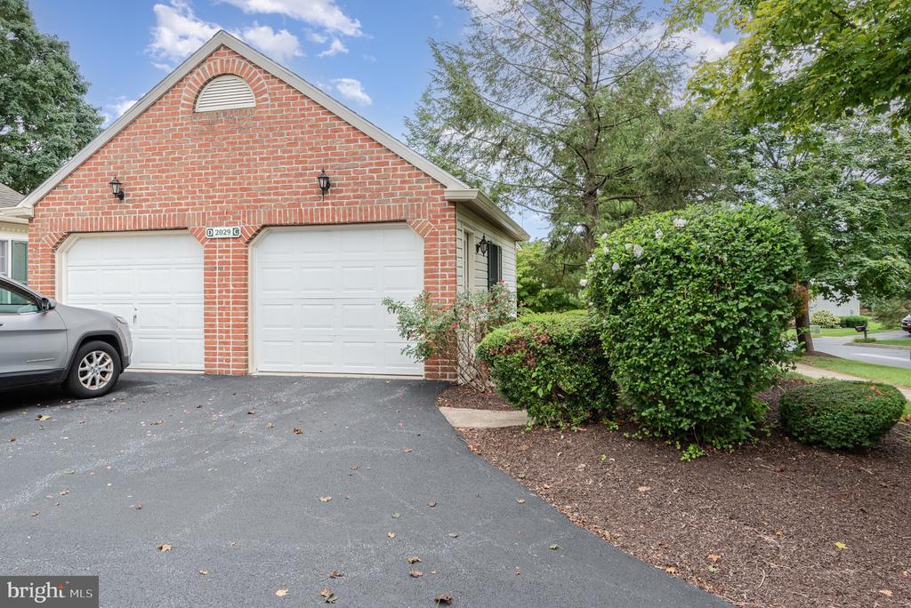 Red brick two-car garage with white doors, an asphalt driveway, and landscaped shrubs.