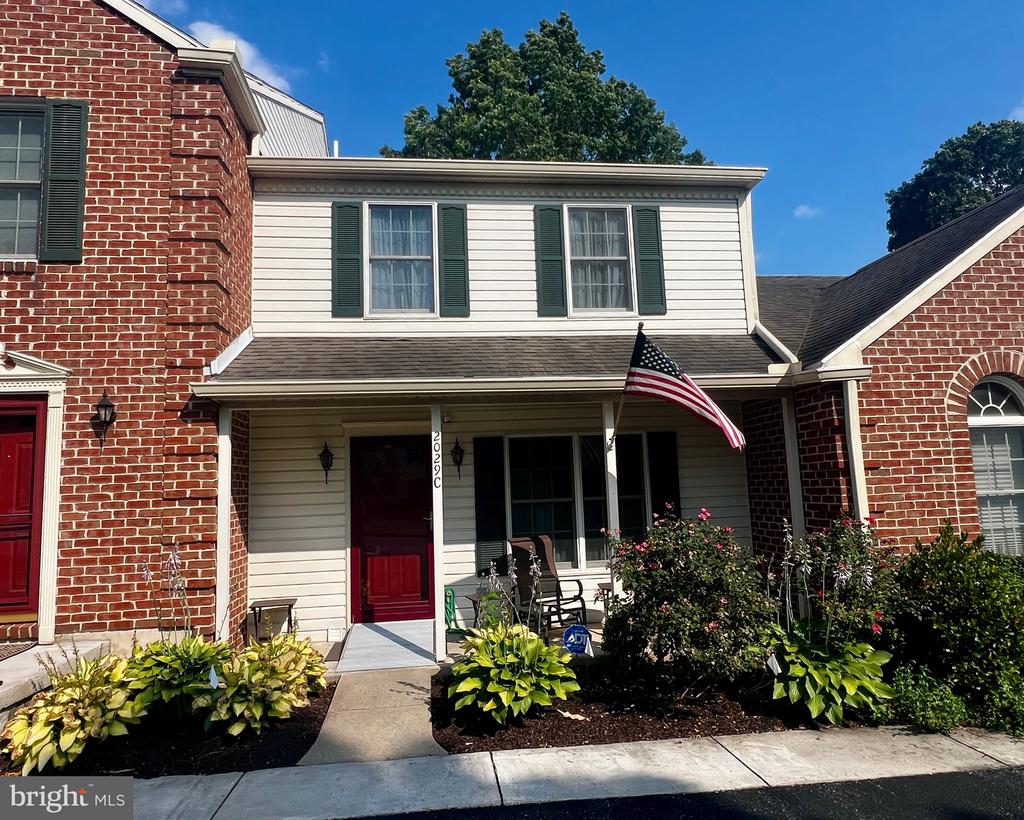 Front exterior of a brick-and-siding home with a covered porch, red door, and American flag.