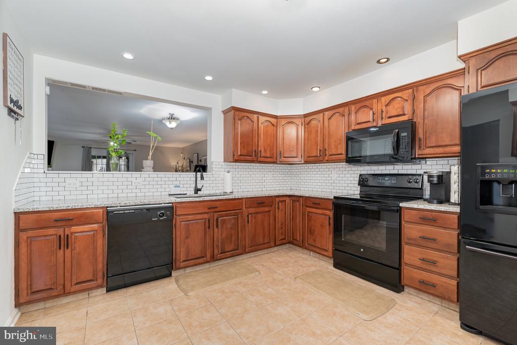 Kitchen with reddish-brown wood cabinets, black appliances, and a wide pass-through to the living area.