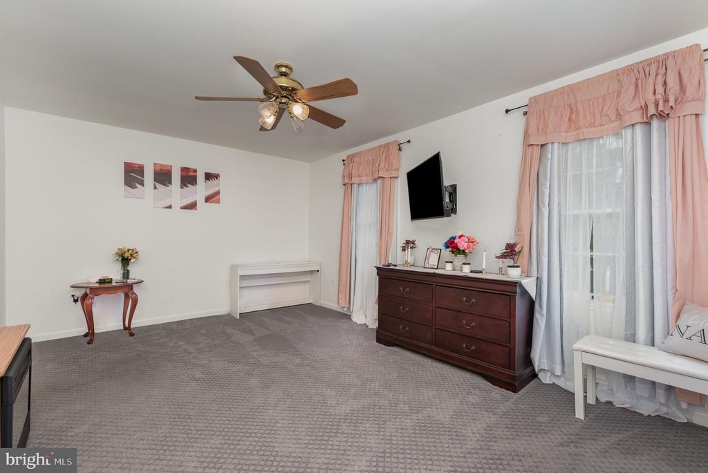 Furnished bedroom with gray carpet, dark wood dresser, ceiling fan, and pink window curtains.
