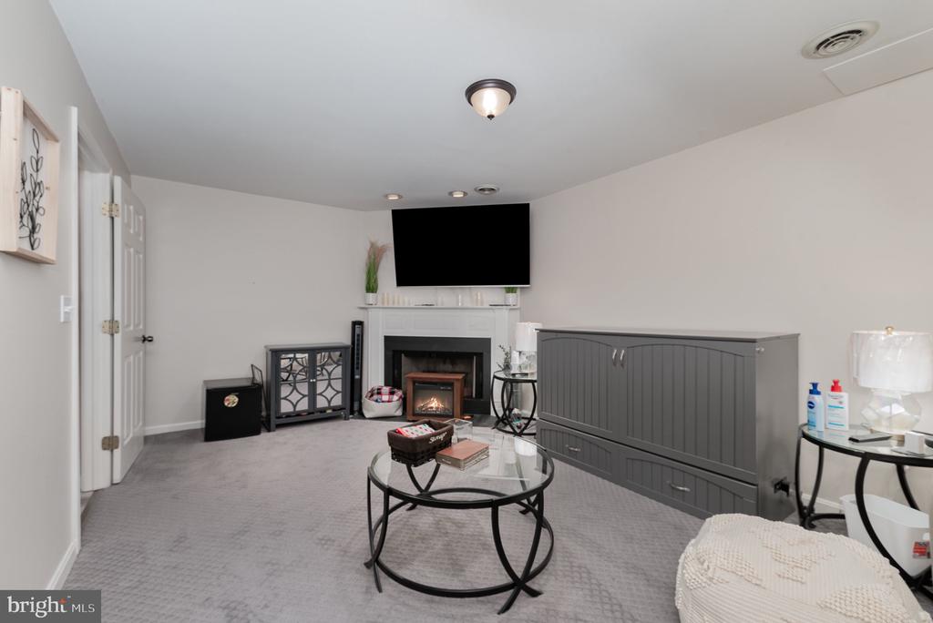 Living room with a white fireplace, wall-mounted TV, gray cabinets, and round glass coffee table.