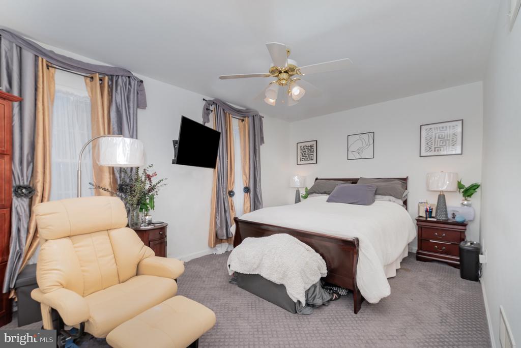 Furnished bedroom with a dark wood bed, beige recliner, and gray-and-gold curtains.