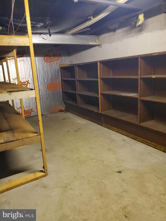 Unfinished basement storage area with built-in wooden shelves and exposed ceiling beams.