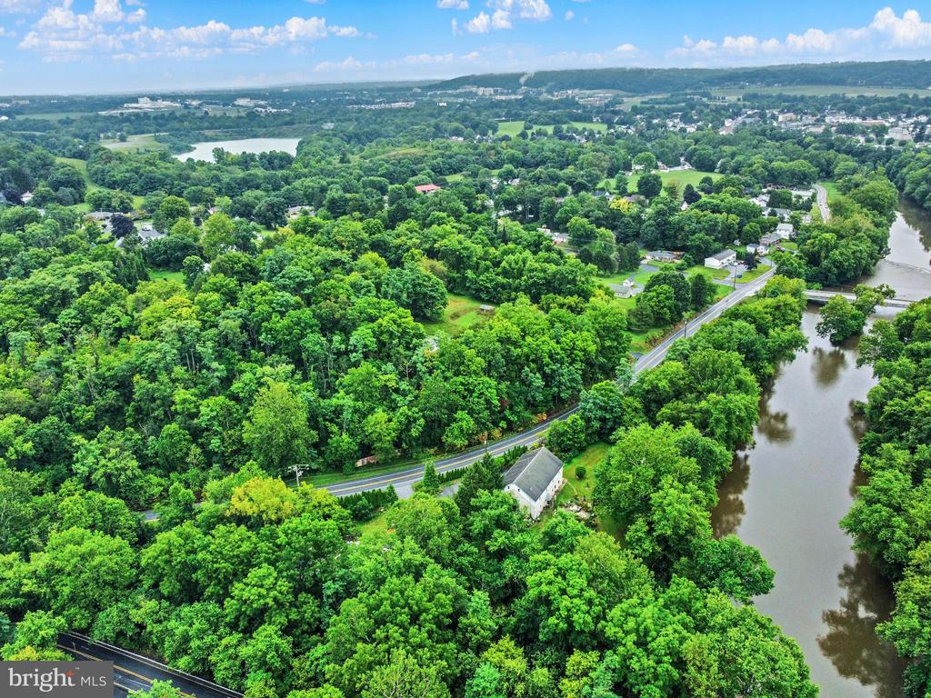 Aerial view of dense woodland along a river, with a road and homes nearby.