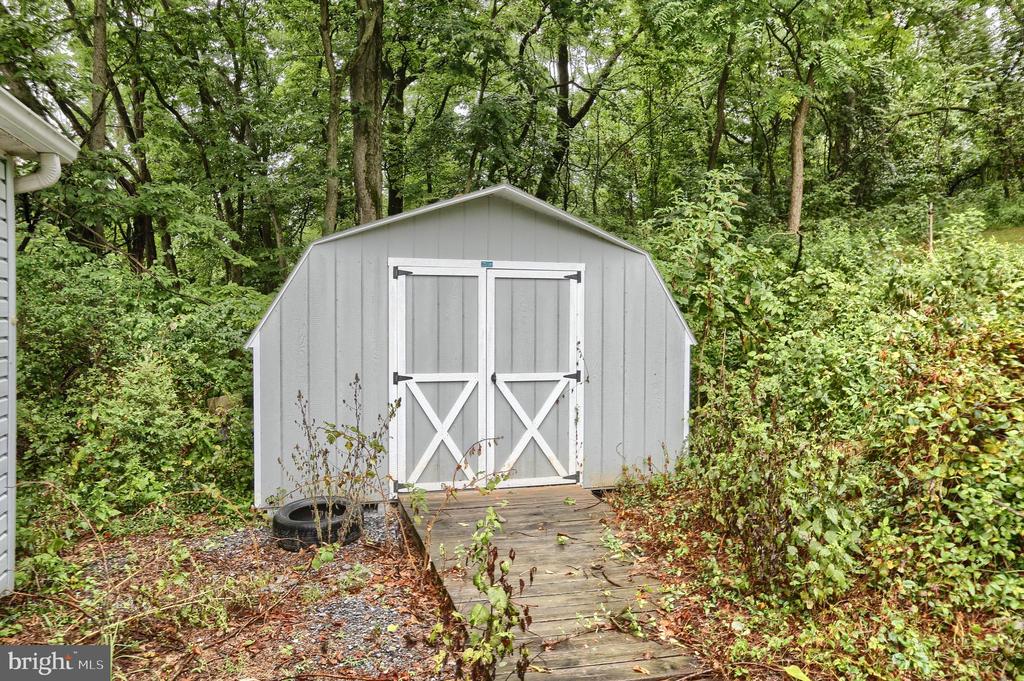 Gray storage shed with white-trimmed double doors in a wooded yard.