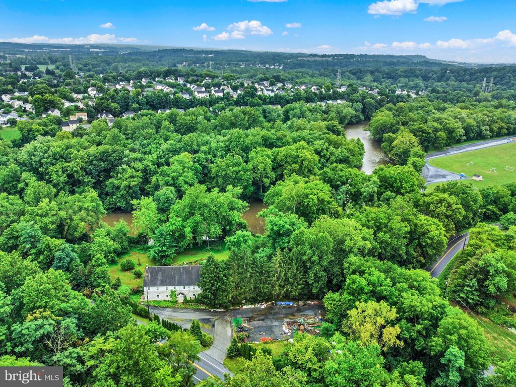 Aerial view of a white house surrounded by trees, with a winding river and neighborhood beyond.
