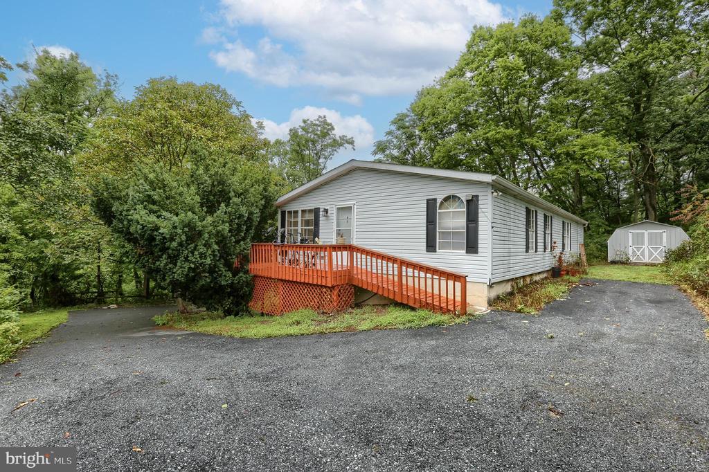 Single-story home with an orange-railed deck and ramp beside a gravel driveway and white shed.