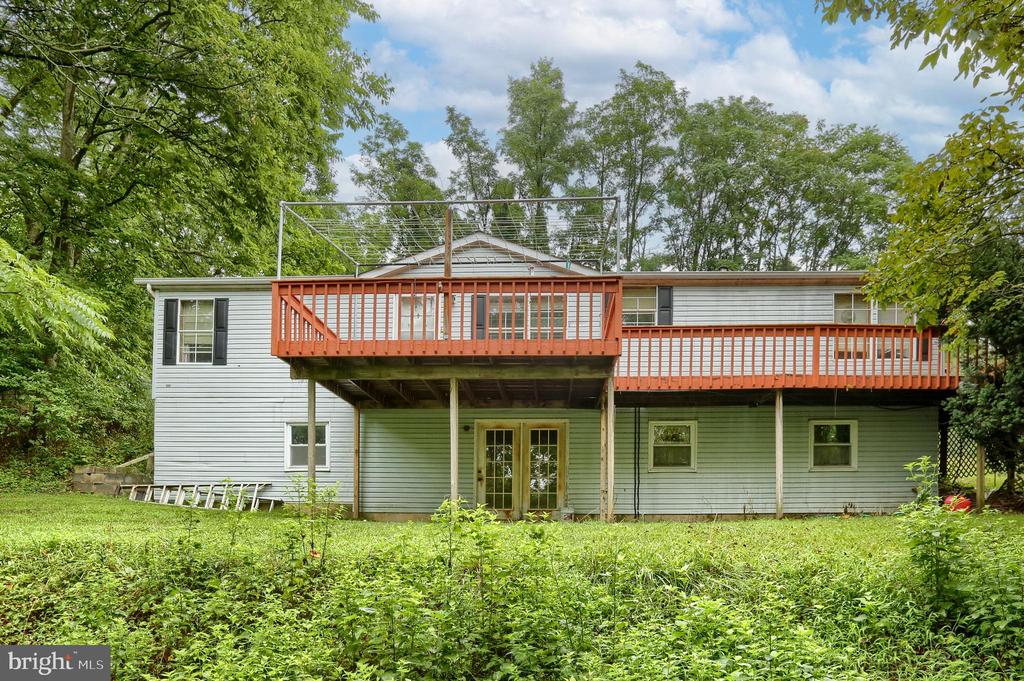 Rear exterior of a gray home with a long red-railed deck and wooded yard.