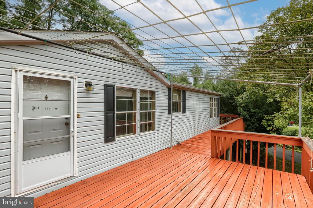 Raised wooden deck with red-stained boards and an overhead trellis beside a gray-sided home.