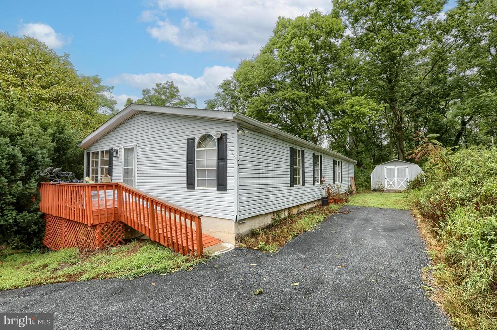 Single-story gray-sided home with a raised deck and ramp beside a paved driveway and storage shed.