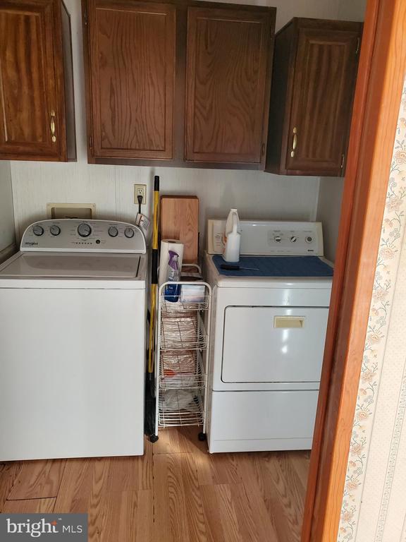Laundry room with a top-loading washer, front-loading dryer, dark wood cabinets, and a narrow wire storage rack.