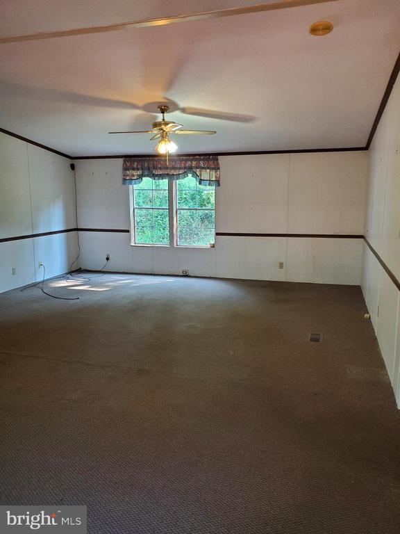 Empty carpeted room with a ceiling fan and a window overlooking greenery.