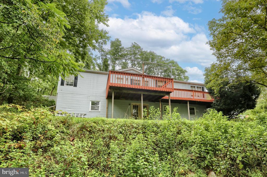 Gray-sided house with a long elevated deck, viewed through dense greenery.