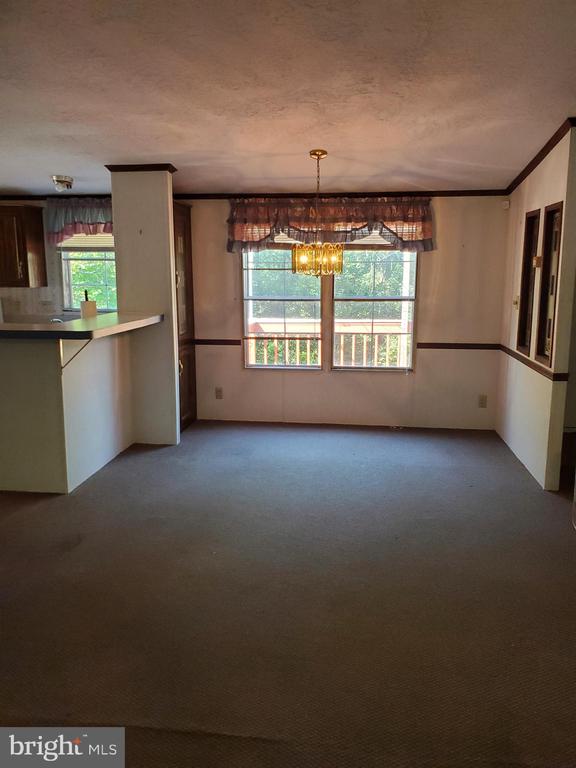 Empty dining area with a brass chandelier, carpeted floor, and windows overlooking a porch.