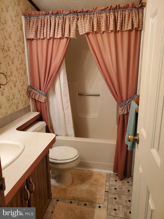 Bathroom with a curtained bathtub, toilet, and vanity beneath floral wallpaper.