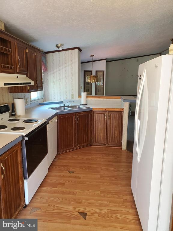 Kitchen with dark wood cabinets, white appliances, and warm-toned plank flooring.