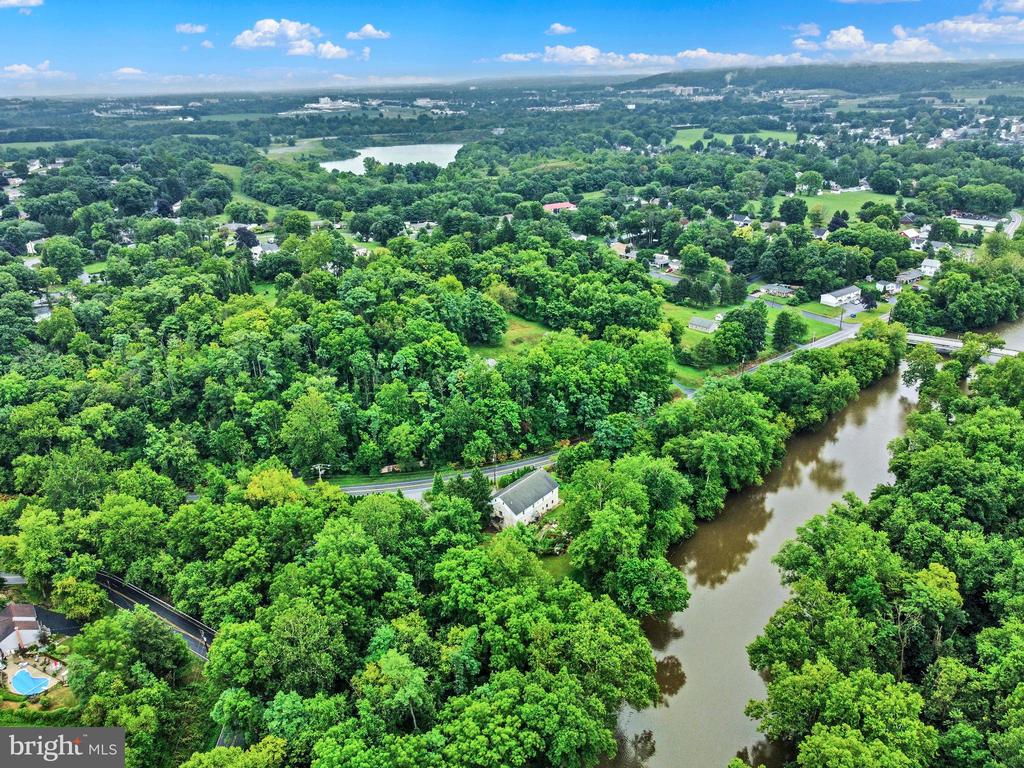 Aerial view of a wooded neighborhood beside a winding river, with distant hills.