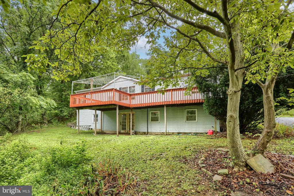 Home’s rear exterior with a large red-railed deck beneath mature trees.